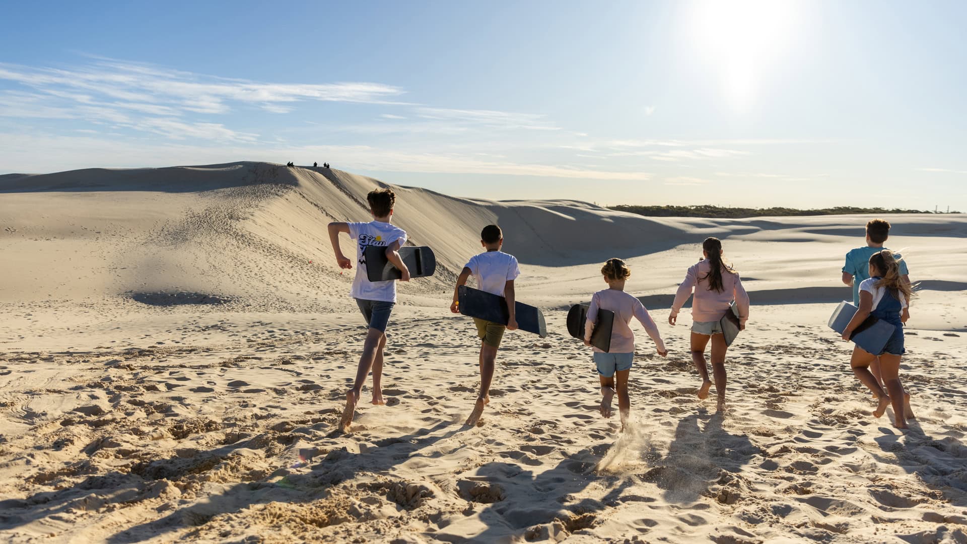 A family enjoys sandboarding during the 4WD R US experience on Stockton Beach Port Stephens Destination NSW